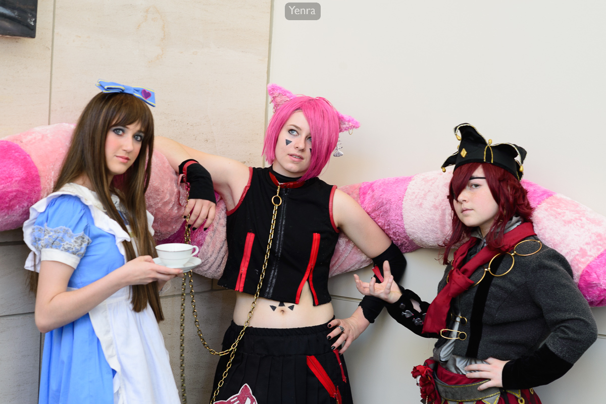 Three individuals dressed in elaborate costumes pose for a photograph against an off-white wall.