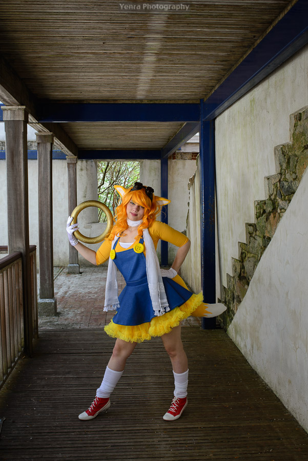 A young woman dressed as Tails from Sonic the Hedgehog stands confidently in an outdoor setting.