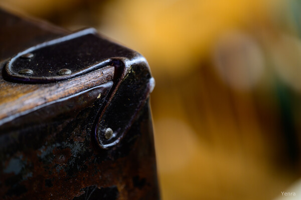 Close-up of a worn leather suitcase corner with riveted straps against a blurred warm background