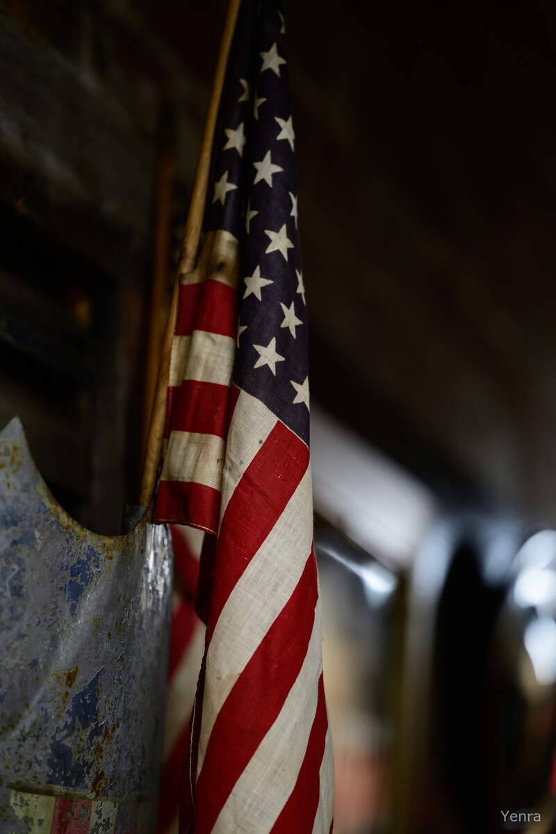 Close-up of a tattered American flag hanging next to a rusty metal object in a dimly lit setting.