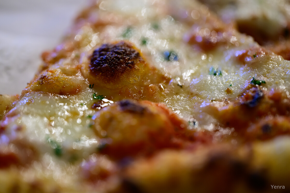 Extreme close-up of pizza slice with melted cheese and herbs
