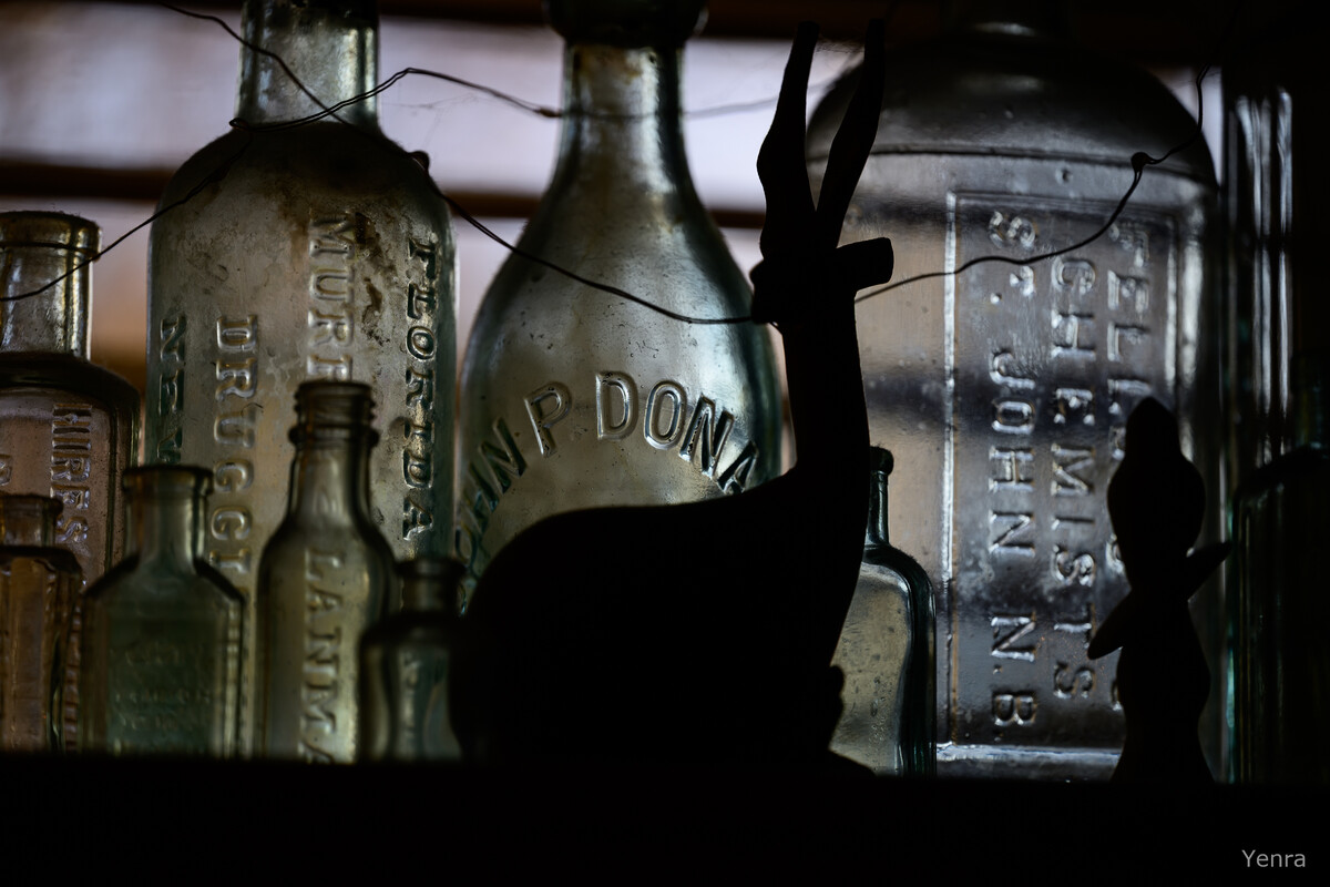 Vintage glass bottles with embossed text on a shelf, partially blocked by the dark silhouette of a deer figurine.