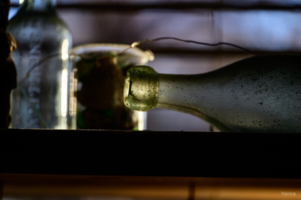 Close-up of a weathered glass bottle lying on its side with a blurred background of other containers.