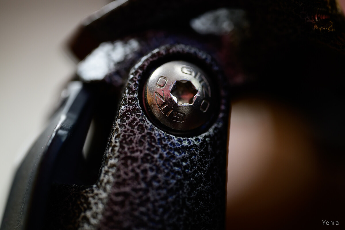 Macro photography of a Gitzo branded screw head on a textured black tripod joint with shallow depth of field.