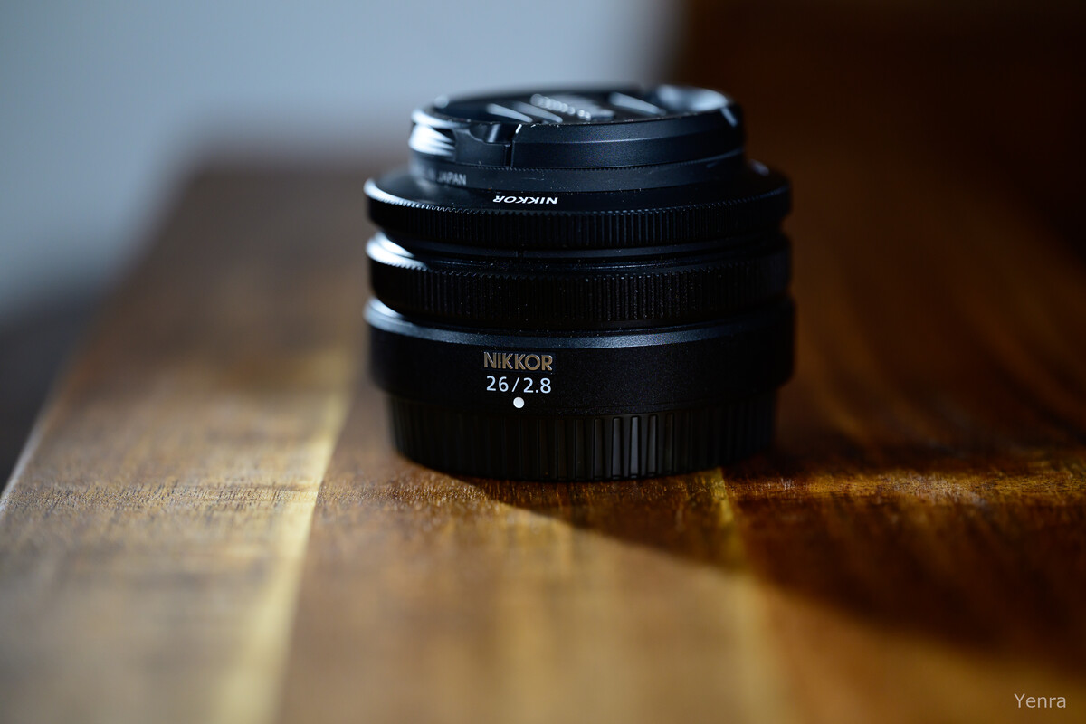Black Nikkor 26mm f/2.8 lens with cap on, resting on a wooden surface