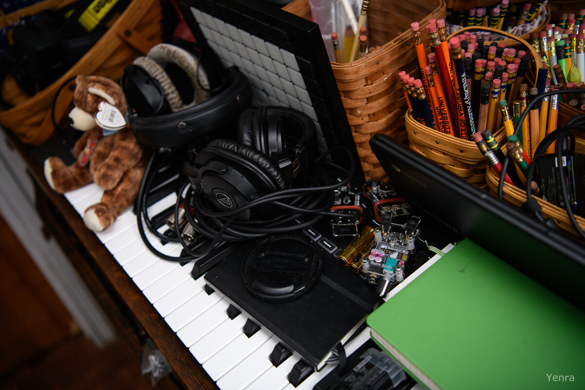 Headphones and electronics cluttered on piano keys next to baskets of pencils
