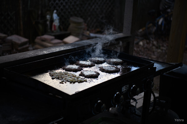 Patties and onions sizzle on a hot outdoor griddle in low light