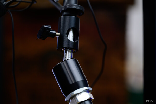 Close-up of a black Manfrotto Magic Arm connection with a locking knob and metallic joint against a blurred background.