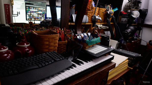 A cluttered desk with keyboards, baskets of writing utensils, and studio lighting equipment.