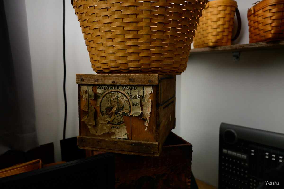 A large woven basket sits on top of a weathered wooden crate with peeling labels, next to a shelf holding other baskets.
