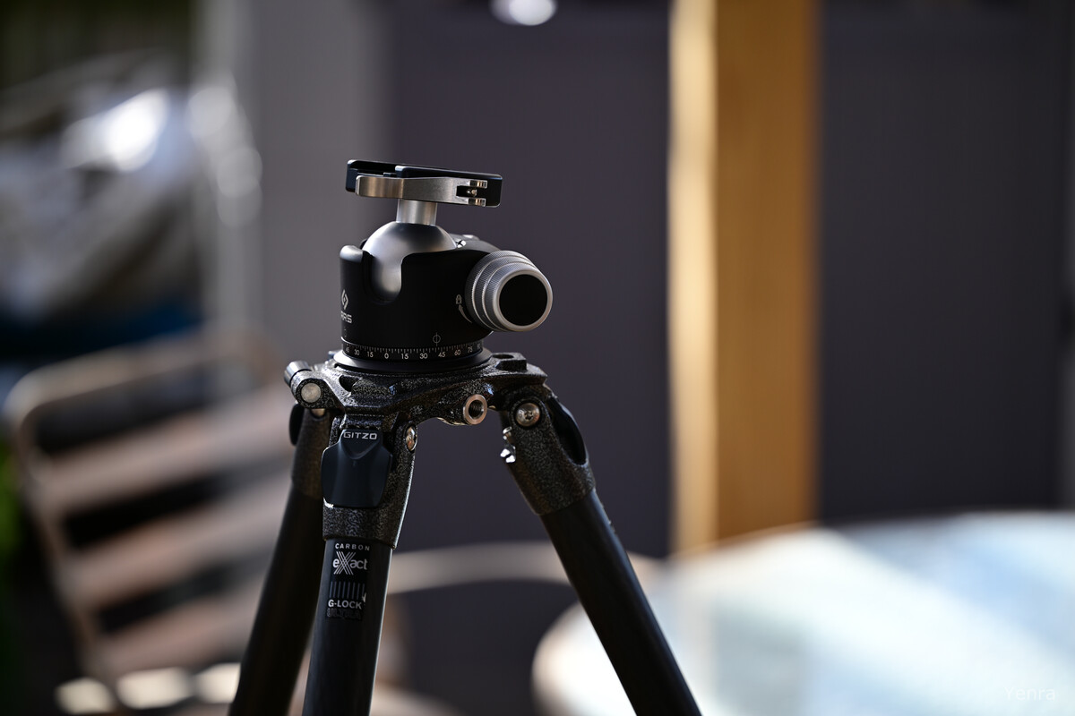Close-up of a black Gitzo carbon fiber tripod with an RRS ballhead against a blurred indoor background.