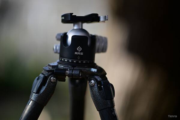 Close-up of an RRS tripod head with fluid dials and a ball mount against a blurred background