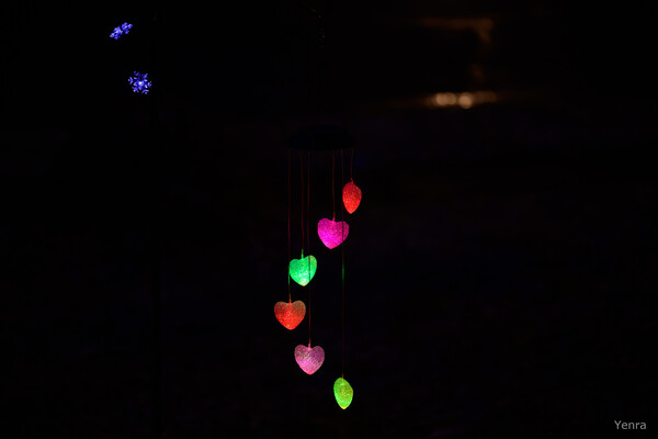 Glowing heart-shaped lights hanging vertically against a dark background with blue floral lights above