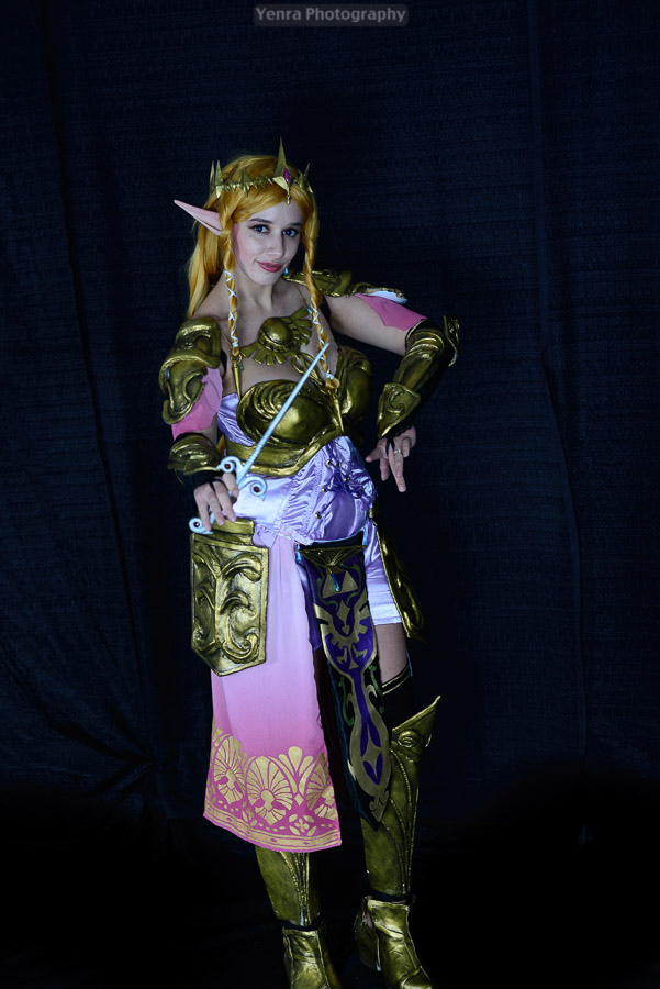 A woman dressed in a fantasy-inspired costume poses for a photograph against a dark blue background.