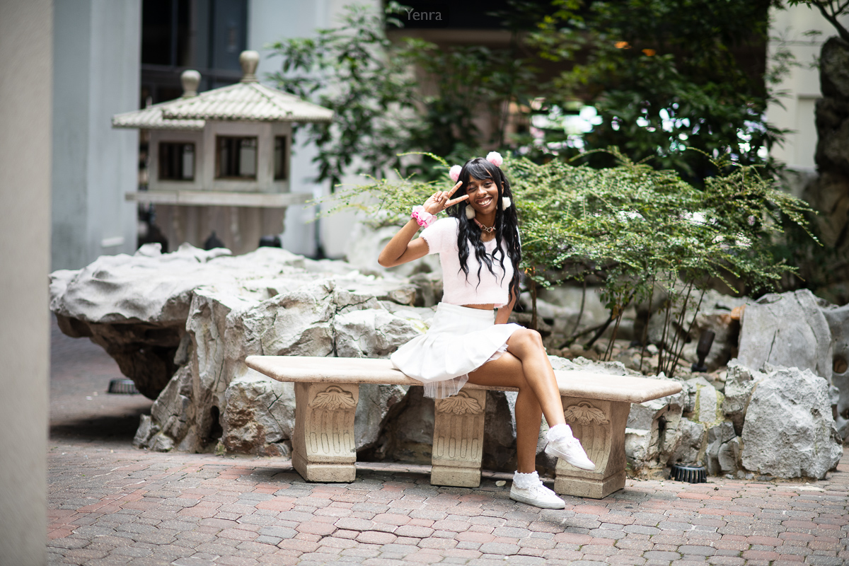 A young woman sitting on a stone bench in front of a rock formation surrounded by greenery.